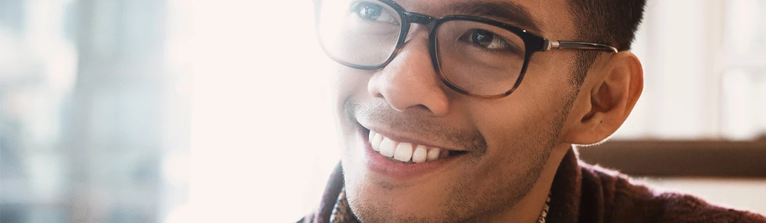 Dentist Wheeling IL Dental Implants Focused a man in glasses is smiling wide while seated in a coffee shop