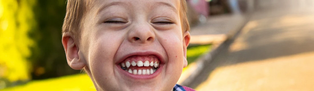 Dentist Wheeling IL Pediatric Dentistry Focused a small boy is laughing joyously with a toothy grin while playing outside